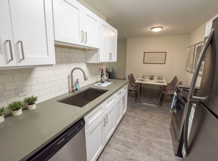 Cook in your gourmet kitchen at Icon Avondale. White cabinets, stainless steel sink, stainless steel dishwasher, stainless steel fridge, dining room table at the end of kitchen, and gray counter tops.